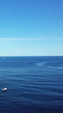 Capo Palinuro, İtalya 'da berrak bir gökyüzünün altında sakin mavi sularda küçük bir tekne ve uzak bir yelkenli manzarası.