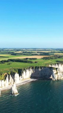 Etretat, Normandiya, Fransa 'nın dramatik beyaz tebeşir kayalıkları ve kıyı şeridi, açık bir gökyüzünün altında mavi deniz ve yeşil tarlalar..
