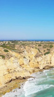 Portekiz 'in Lagos yakınlarındaki Algarve kıyısı boyunca açık mavi gökyüzünün altında dramatik altın uçurumlar ve turkuaz dalgalar görülüyor..