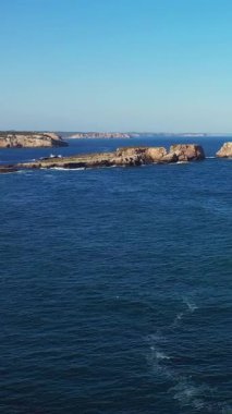 Açık mavi okyanus, parlak bir gökyüzünün altında Sagres, Portekiz yakınlarındaki Algarve kıyısında kayalık çıkıntılar var. Sakin deniz manzarası seyahat ve doğa kavramları için idealdir..