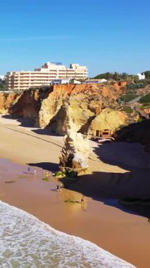 Portekiz 'in Albufeira kenti yakınlarındaki Algarve sahilindeki kumlu bir plajda dramatik kayalıklar ve kaya oluşumları yükseliyor..