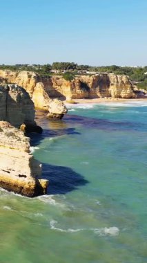 Algar de Benagil, Algarve, Portekiz 'deki sahil boyunca uzanan berrak turkuaz suların üzerinde dramatik altın kayalıklar yükselir. Parlak güneş ışığı, engebeli kaya oluşumlarını ve aşağıdaki sakin plajı vurguluyor..