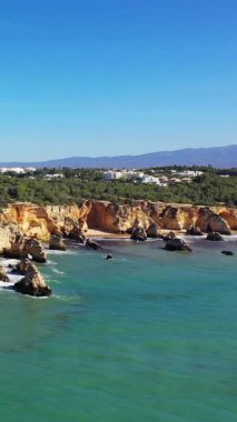 Albufeira yakınlarındaki Algarve sahil şeridinin dramatik uçurumları, turkuaz suyu ve berrak mavi gökyüzü manzarası. Engebeli kaya oluşumları ve yemyeşil yemyeşil resim gibi bir kıyı manzarası yaratır..