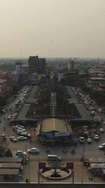 Kamboçya 'da şehir binaları ve trafik ile çevrili, hareketli Battambang pazarının yüksek açılı görüntüsü, gün batımında sisli bir gökyüzü ile yakalandı..