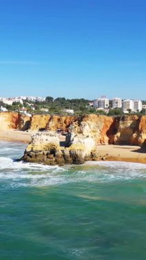 Portekiz 'in Albufeira kenti yakınlarındaki Algarve sahilinde kumlu bir sahil boyunca dramatik uçurumlar ve turkuaz dalgalar var..