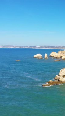 Portekiz 'in Albufeira yakınlarındaki Algarve kıyı şeridi boyunca uzanan engebeli uçurumlar ve turkuaz okyanus manzarası berrak mavi bir gökyüzünün altında..