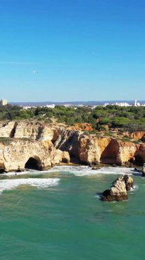 Portekiz 'in Albufeira yakınlarındaki Algarve kıyı şeridi boyunca açık mavi bir gökyüzünün altında dramatik kireçtaşı kayalıkları ve turkuaz suları..