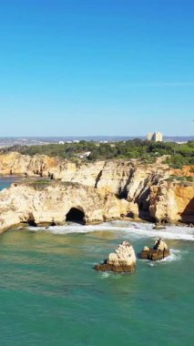 Portekiz 'in Albufeira yakınlarındaki Algarve kıyı şeridi boyunca uzanan engebeli uçurumların ve turkuaz suların manzarası berrak mavi bir gökyüzünün altında..