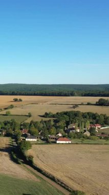 Kırsal alanların manzaralı manzarası ve Fransa 'nın Cuncy les Varzy şehrinde açık mavi bir gökyüzünün altında küçük bir köy. Arka planda orman olan sakin tarım arazisi.