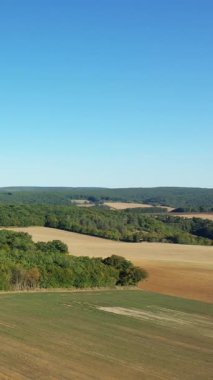 Fransa 'da Cuncy les Varzy yakınlarında açık mavi bir gökyüzü altında yuvarlanan tarlaların ve yoğun yeşil ormanların manzarası. Huzurlu kırsal alan doğa ve kırsal konular için ideal.