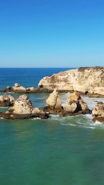 Portekiz 'in Albufeira yakınlarındaki Algarve kıyısındaki turkuaz sulardan, berrak mavi gökyüzünün altında dramatik kireçtaşı oluşumları yükseliyor..