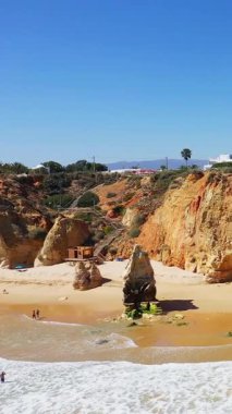 Dramatik altın uçurumları, eşsiz kaya oluşumları ve Portekiz 'in Algarve bölgesindeki kumlu plajın tadını çıkaran insanlarla dolu güneşli sahil sahnesi..