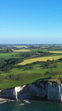 Etretat 'ın ikonik beyaz tebeşir uçurumlarının sersemletici hava manzarası yemyeşil tarlaları ve Fransa' nın Normandiya şehrinde açık mavi bir gökyüzünün altına uzanan tarım arazileri..