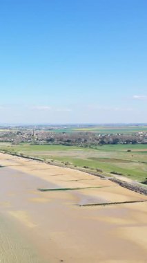 Bernieres-sur-Mer, Fransa 'daki Juno Sahili' nin geniş hava görüntülerinde kumlu kıyı şeridi, yeşil tarlalar ve açık mavi gökyüzünün altındaki uzak bir köy görülüyor..