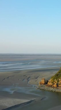 Kenarında küçük bir taş bina bulunan geniş kumlu gelgit düzlükleri, Fransa 'nın Le Mont-Saint-Michel kentinde alçak gelgitte yakalandı..