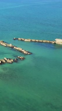 Gold Beach, Asnelles, Normandiya, Fransa yakınlarındaki turkuaz sularda bulunan yapay bir limanın beton kalıntıları. Tarihi yapılara ve canlı renklere sahip sakin deniz manzarası.