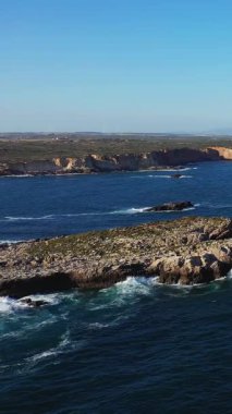 Portekiz 'in Algarve bölgesinde Sagres yakınlarında açık mavi bir gökyüzü altında kayalıklara çarpan dramatik kayalık kıyı şeridi.