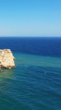 Portekiz 'in Lagos kenti yakınlarındaki Algarve kıyısında parlak bir gökyüzünün altında engebeli uçurumların ve berrak mavi okyanusun manzarası. Seyahat ve doğa kavramları için mükemmel..