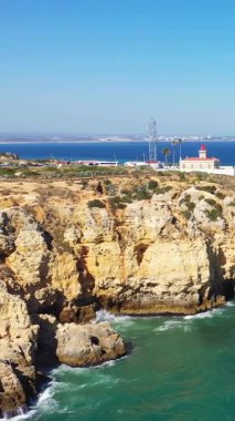 Portekiz 'in Lagos kenti yakınlarındaki Algarve kıyısı boyunca turkuaz Atlantik Okyanusu' na bakan dramatik altın uçurumlar ve deniz feneri güneşli bir günde.