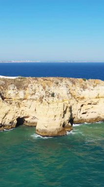 Portekiz 'in Lagos yakınlarındaki Algarve kıyısındaki berrak turkuaz suların üzerinde parlak mavi bir gökyüzünün altında dramatik kireçtaşı kayalıkları yükseliyor..