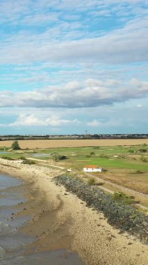 Kırsal bir kıyı şeridi manzarası, kumlu kıyılar, yeşil alanlar ve parçalı bulutlu bir gökyüzü. Doğal dokuları ve açık alanı olan huzurlu kırsal atmosfer.