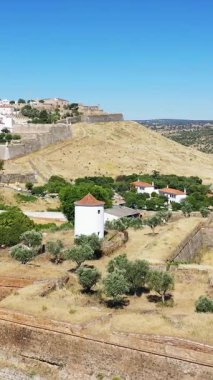 Portekiz, Elvas 'taki tarihi tahkimatların ve beyazlatılmış binaların açık mavi gökyüzünün altında havadan görünüşü. Sahnede savunma duvarları, küçük yuvarlak bir kule ve Akdeniz bitkileri yer alıyor..