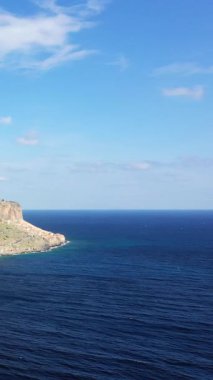 Yunanistan 'ın Monemvasia kentinde açık bir gökyüzünün altında derin mavi denizle buluşan kayalık bir kıyı kayasının manzarası. Seyahat ve doğa kavramları için ideal huzurlu doğal manzara..
