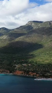 Yunanistan 'ın Monemvasia kenti yakınlarındaki yemyeşil verimli bir sahil ve engebeli bir dağ kıyı şeridi manzarası. Dramatik bulutlar manzarayı gölgeleyerek sakin ve doğal bir atmosfer yaratıyor..