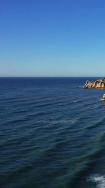 Açık bir gökyüzü altında Portekiz 'in Lagos yakınlarındaki Algarve kıyısı boyunca yumuşak dalgalar ve engebeli uçurumlarla derin mavi Atlantik Okyanusu' nun geniş manzarası..