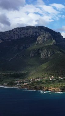 Yunanistan 'ın Monemvasia kenti yakınlarındaki yemyeşil ve mavi deniz manzaralı engebeli dağlar ve kıyı şeridi, parçalı bulutlu bir gökyüzü altında..