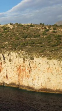 Yunanistan 'ın Mani bölgesindeki Diros Sahili yakınlarındaki engebeli uçurumların ve kayalık kıyı şeridinin manzarası. Manzara, sakin mavi suyun üzerinde dokulu kaya oluşumları ve seyrek bitki örtüsüne sahiptir..