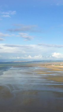 Lion-sur-Mer, Normandiya 'daki Sword Beach' in geniş panoramik manzarası. Islak kum, sığ su ve parçalı bulutlu gökyüzü. Huzurlu kıyı manzarası Fransız sahil şeridinin dingin güzelliğini yansıtıyor..