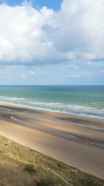 Fransa 'nın Normandiya şehrinde bulutlu bir gökyüzünün altında yumuşak dalgalar ve kumlu kıyı şeridi ile geniş bir manzara..
