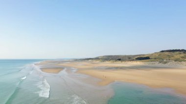 Fransa, Plage de la Vieille eglise 'de açık mavi gökyüzü altında yumuşak dalgalar ve uzak kumullarla geniş kumlu bir sahil. Huzurlu kıyı manzarası doğa ve seyahat temaları için ideal.