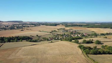 Fransa 'nın Cuncy les Varzy kentindeki temiz mavi gökyüzünün altında kırsal alanların ve köyün insansız hava aracı görüntüleri. Geniş tarım alanları ve dağınık ağaçlar huzurlu bir manzara yaratır..
