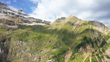 Güneşli yeşil yamaçlar ve Gavarnie Sirki 'nde engebeli uçurumlar, Fransız Pireneleri, parçalı bulutlu bir gökyüzünün altında.