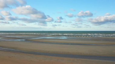 Normandiya, Fransa 'daki Utah Sahili' nin geniş bir manzarası. Islak kum, hafif dalgalar ve parçalı bulutlu bir gökyüzü. Huzurlu deniz manzarası bu tarihi kıyı bölgesinin doğal güzelliğini vurguluyor..
