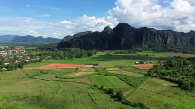 Vang Vieng, Laos yakınlarındaki mavi gökyüzünün altında yeşil tarlaların ve dramatik kireçtaşı dağlarının havadan görünüşü. Çiftlik arazisi ve doğal güzelliği olan kırsal manzara.