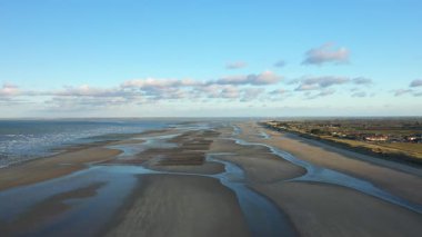 Fransa 'nın Normandiya kentindeki Utah Sahili' nde açık mavi gökyüzünün altında geniş kumlu sahilin ve gelgit desenlerinin hava görüntüsü. Huzurlu sahne doğal dokuları ve kıyı güzelliğini vurguluyor..