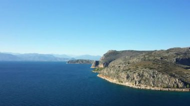 Yunanistan 'ın Nafplio kentinde açık bir gökyüzü altında kayalık kıyı şeridi ve derin mavi denizin manzarası. Engebeli kayalıklar sakin sularla buluşarak sakin bir Akdeniz manzarası yaratıyor..