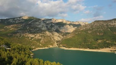 Fransa 'nın güneyindeki Gorges du Verdon' un turkuaz gölü ve dramatik uçurumları, yemyeşil tepeler ve parçalı bulutlu bir gökyüzünün altında kumlu bir kıyı şeridi..