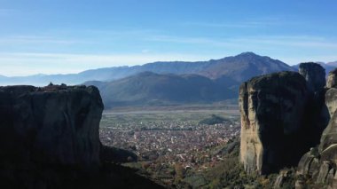 Yunanistan 'ın Meteora bölgesinde açık mavi gökyüzünün altındaki uzak dağlara bakan yüksek kaya oluşumlarına geniş bir bakış açısı.