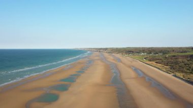 Geniş kumlu kıyı şeridi ve açık gökyüzünün altındaki Omaha Sahili, Normandiya 'daki mavi denizin havadan görünüşü. Manzara yumuşak dalgalar ve barışçıl, doğal bir ortam içerir..