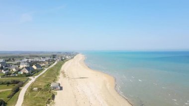 Açık güneşli bir günde, Fransa 'nın Normandiya eyaletindeki Utah Sahili' ndeki kumlu sahil ve kıyı köyünün insansız hava aracı görüntüsü. Sakin deniz manzarası, mavi gökyüzü ve sakin sular..