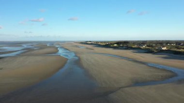 Fransa 'nın Normandiya eyaletindeki Utah Sahili' nde açık mavi gökyüzünün altında sığ gelgit havuzları olan geniş kumlu bir kıyı şeridi. Uzak evleri ve açık ufku olan kıyı manzarası.