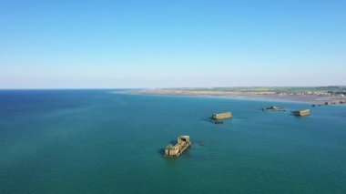 Gold Beach, Asnelles, Normandiya, Fransa yakınlarındaki deniz manzaralı tarihi yapay liman yapıları, açık mavi bir gökyüzü ve arka planda kıyı şeridi ile.