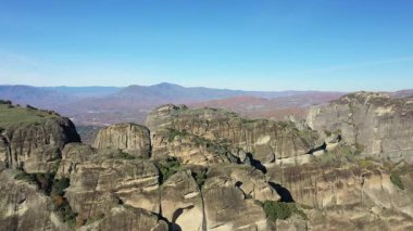 Yunanistan 'daki açık mavi gökyüzü altındaki dramatik Meteora kayalıklarının hava manzarası benzersiz kaya oluşumları ve uzak dağları gösteriyor.