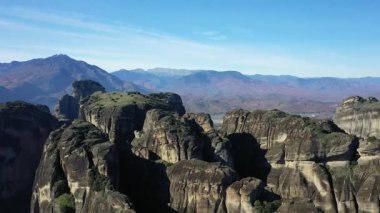 Yunanistan 'da açık mavi gökyüzü altında engebeli kaya oluşumlarıyla çarpan Meteora kayalıklarının hava manzarası. Uzak dağlar ve sonbahar renkleriyle görkemli manzara.