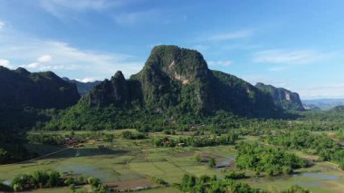Açık bir günde Laos kırsalında dramatik yeşil dağların ve sel basmış pirinç tarlalarının havadan görünüşü. Geleneksel köy evleri tarlalar ve ormanlar arasında dağıtılmıştır..