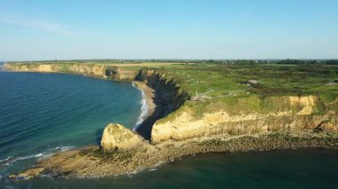 Fransa 'nın Pointe du Hoc kentindeki engebeli uçurumların ve kıyı şeridinin havadan görünüşü yeşil tarlalar ve açık mavi bir gökyüzü altında.